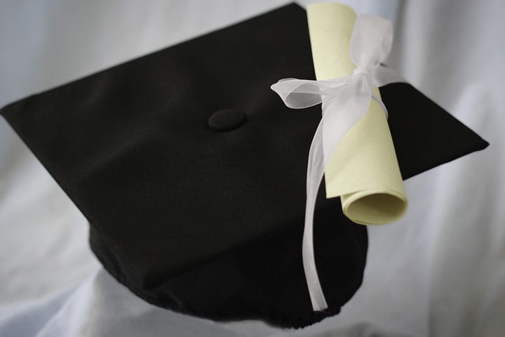 A scroll lays on top of a graduation cap