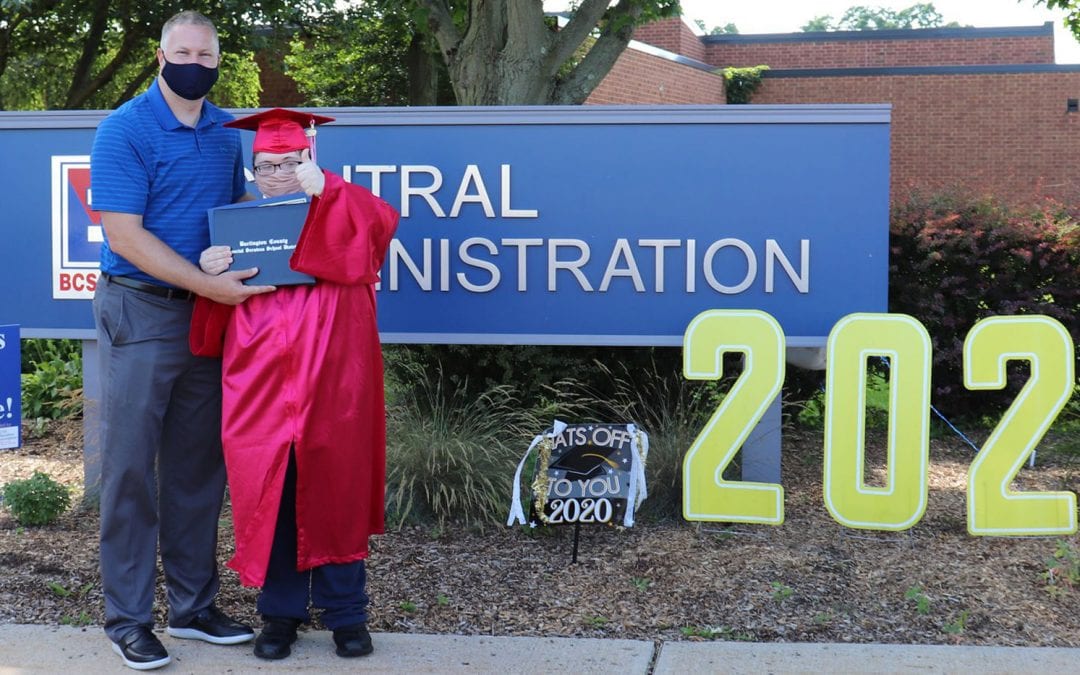 BCSSSD Principal Ryan Varga and Transition Campus graduate Noah, who is excitedly wearing his cap and gown, as they pose while wearing masks for a picture outside of the school.