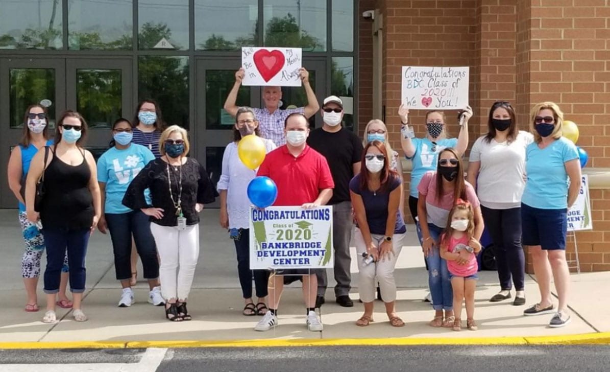 Teachers and staff gather outside of Gloucester County Special Services School District with signs, masks and balloons congratulating their graduates.