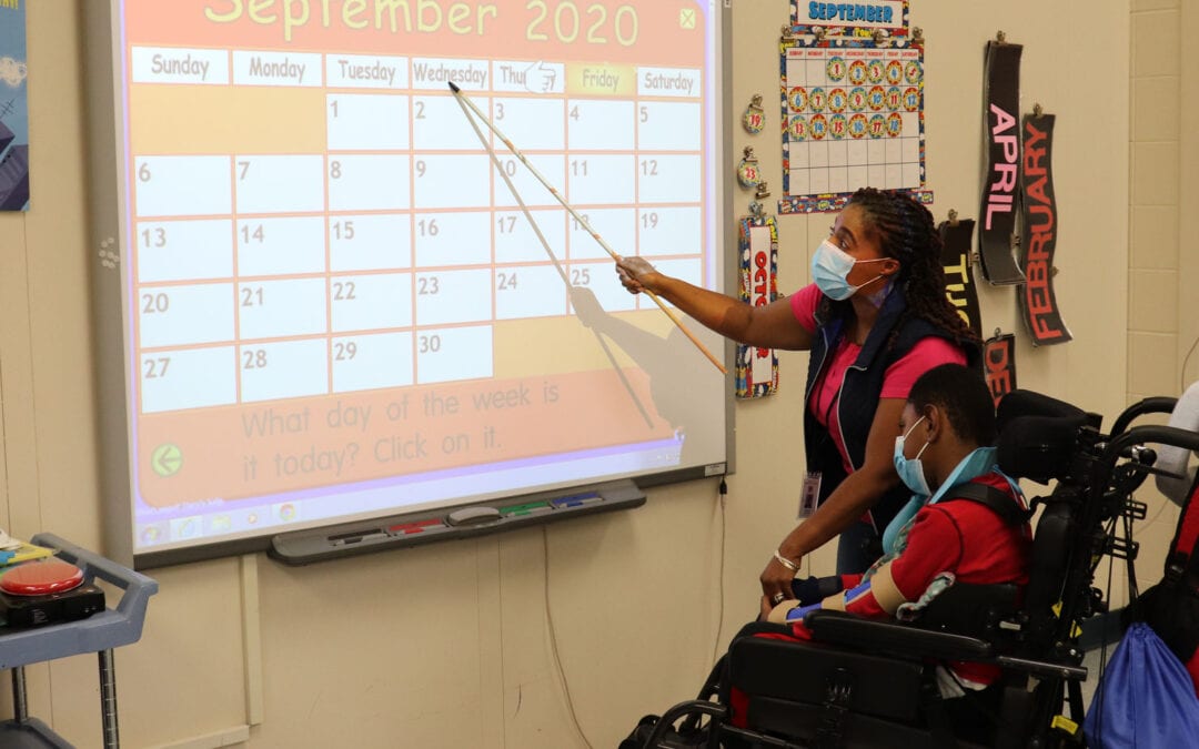 Sharonda Stevens, a teacher at Burlington County Special Services School District, points to a large calendar as she helps a student learn the different days of the week.