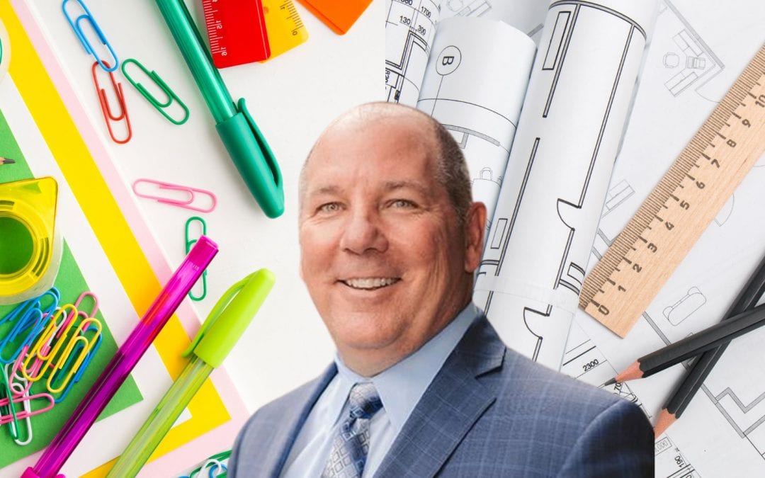 Dr. Joseph Flynn, now retired from Warren County Special Services School District, smiles in a photo that is surrounded by school supplies and architecture blueprints