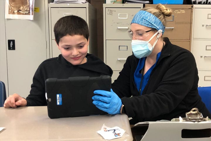 Rachel Krementz, a teacher with Cape May Special Services School district, wears a mask and gloves as she assists one of her students as he learned on an iPad