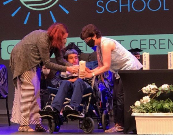 ACSSSD staff members assist a graduate on stage during the commencement ceremony.