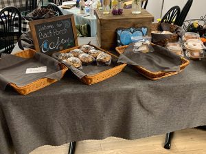 Baked goods are displayed in baskets on a table with a chalkboard sign that reads Welcome to the Back Porch Cafe.