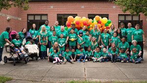 A large group of students and staff members in green shirts pose outside the Joseph F. Capello school with yellow, orange, and green balloons behind them as they are honored for their partnership with Jersey Fresh.