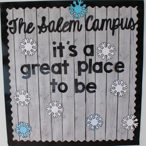 A bulletin board in the entryway is decorated with a gray wooden background, white and blue snowflakes, and it reads The Salem campus it’s a great place to be. 