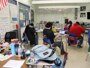 Five students are seated in a classroom, each at their own desk and working on their Chromebook. 