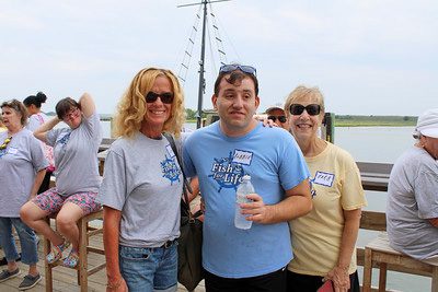 Two women in sunglasses stand on either side of a young man standing on a dock.