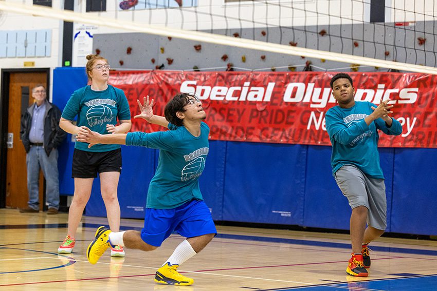 Three students are playing volleyball in a school gym.