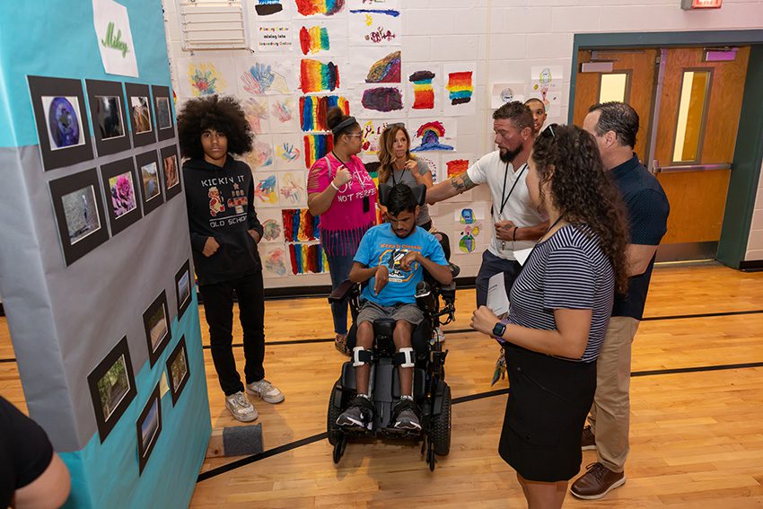 Students and staff gather around colorful student artwork displays in the school gym