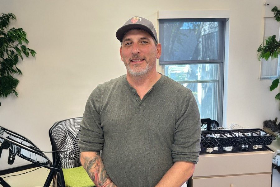 A male teacher wearing a baseball cap stands in his classroom.