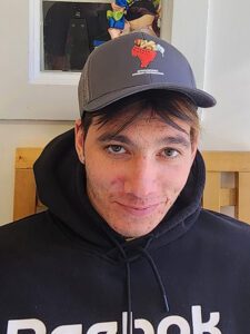 A male student wearing a baseball cap is smiling in his classroom.