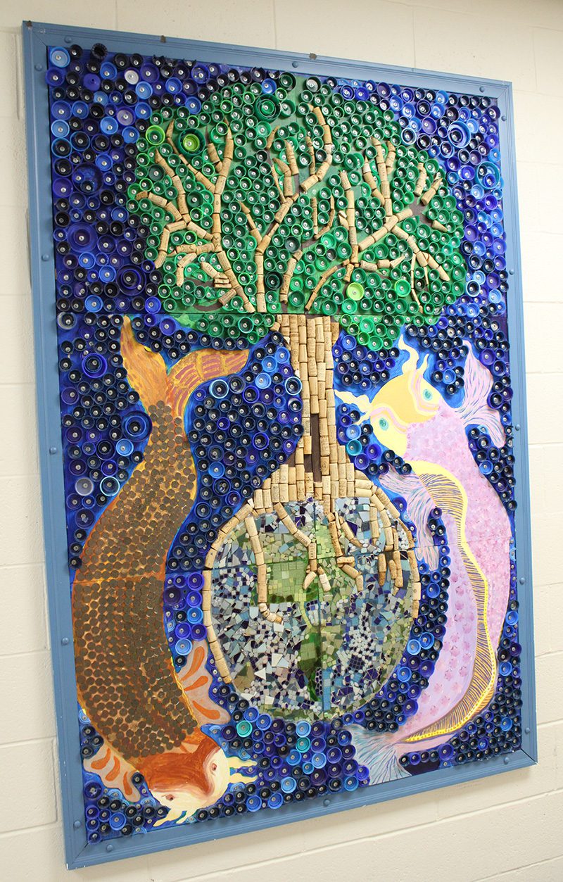 A bulletin board has a combination of rolled paper, cork, and paintings that depict a tree with two koi fish swimming around the root ball.