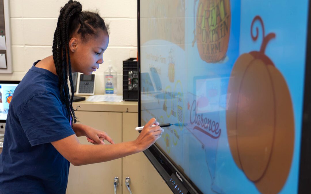 A student is using a stylus to do a pumpkin activity on a large interactive touch screen.