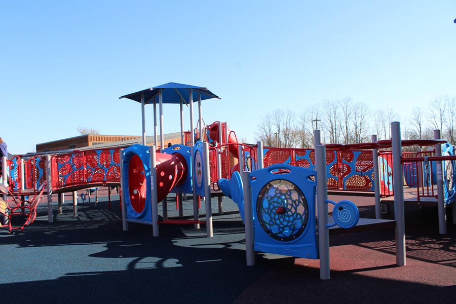 A new playground with a rubber ground surface sits outside the school, while staff members supervise the students playing. 