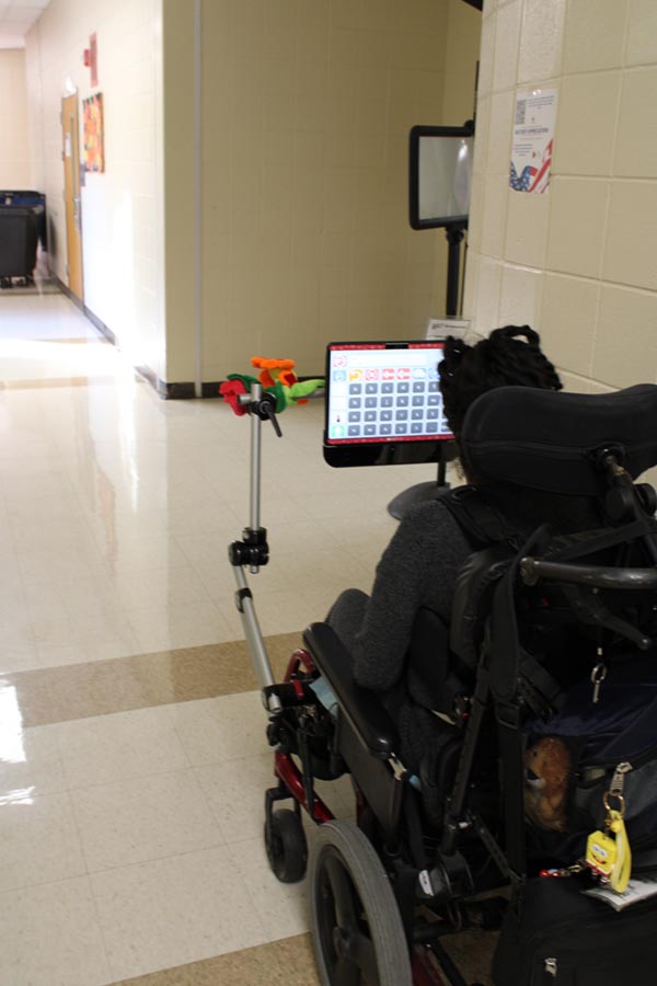 A student in a wheelchair faces her electronic communication device that depicts squares that represent words.