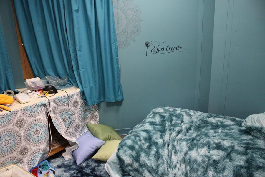 A blue room with a Just Breathe sticker on the wall and pillows has dim lighting and a plush rug.